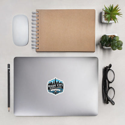 Windy City logo sticker, 3 by 3 inches, on a laptop beside a notebook and glasses