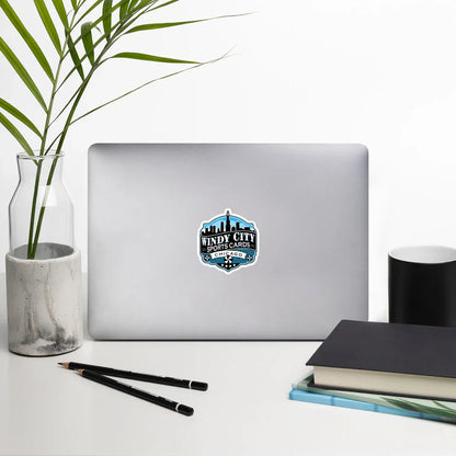 Windy City logo sticker, 4 by 4 inches, on a laptop beside books and a plant