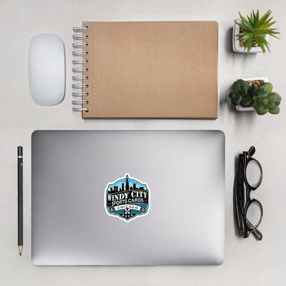 Windy City logo sticker, 5.5 by 5.5 inches, on a laptop beside a notebook and glasses