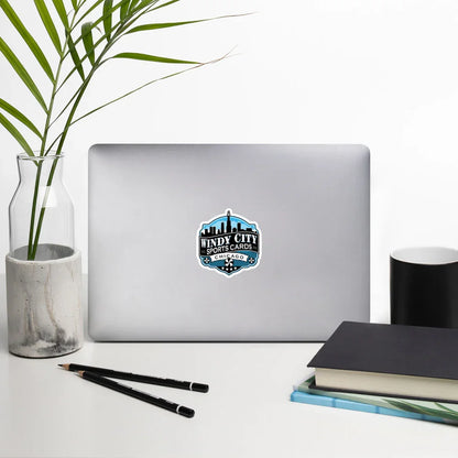 Windy City logo sticker, 5.5 by 5.5 inches, on a laptop beside books and a plant